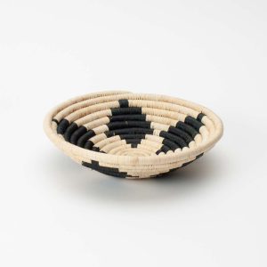 Seitenansicht einer handgemachten runden Schale aus Raffiabast, hergestellt in Ruanda, auf einem weissen Hintergrund. Der Korb hat ein schwarz-beiges geometrisches Muster.