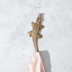 Ein Wandhaken aus recyceltem Messing, der aussieht wie ein Krokodil. An seinem Schwanz hängt ein Handtuch.